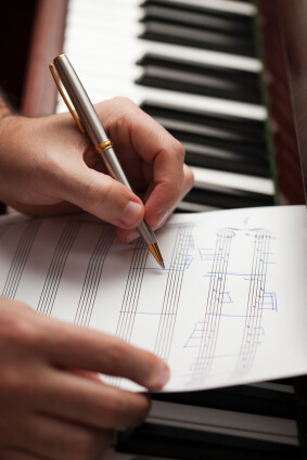 A White person's hand writing with a pen on some sheet music placed on top of the keys of a piano.