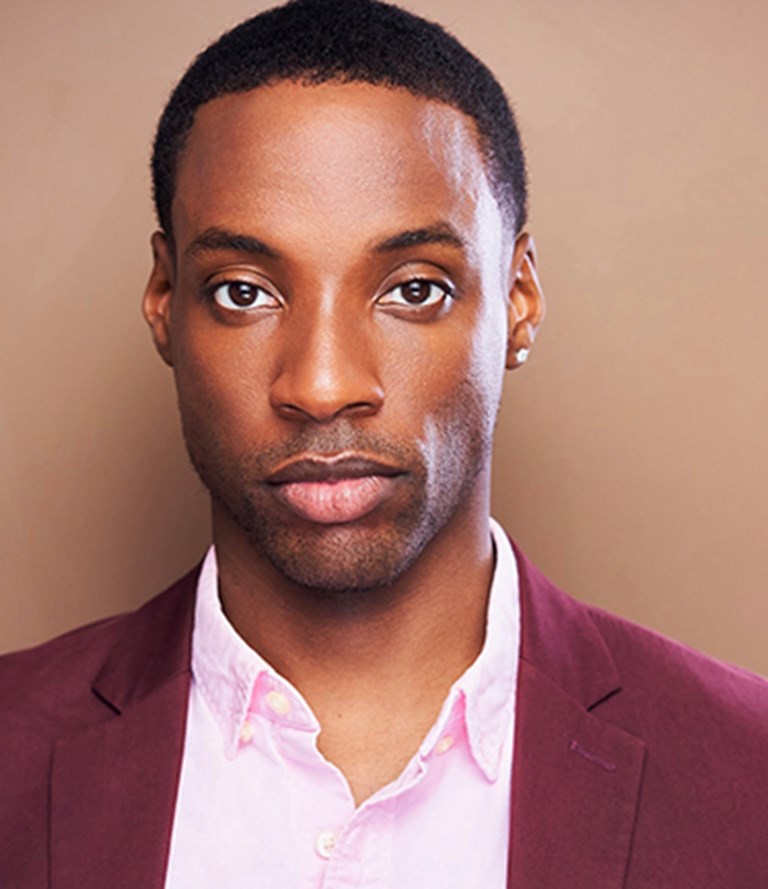 Christian Mark Gibbs in a maroon blazer an unbutton light pink collared shirt.