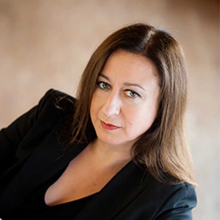 Conductor Simone Young leaning over a red leather couch wearing in a black "V" neck blouse and matching suit.