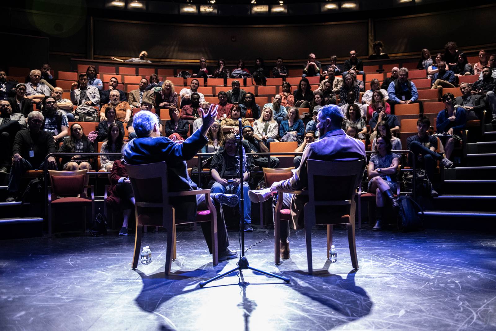 An audience of college students watches a Latino man interviewed onstage.