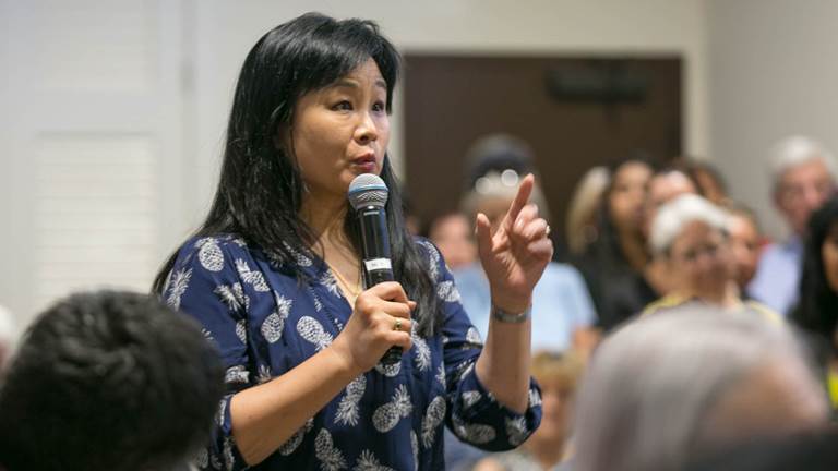 A woman uses a handheld microphone to ask a question at a town hall 