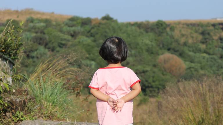 A young girl looks out at the hills and trees in front of her