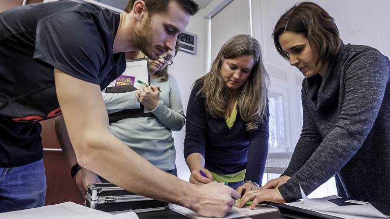 Four teachers stand around a table and work together on a piece of paper