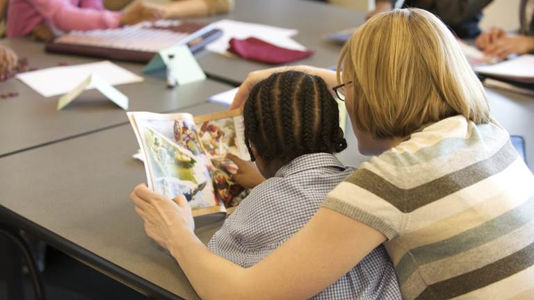An adult volunteer reads a comic book with a child 