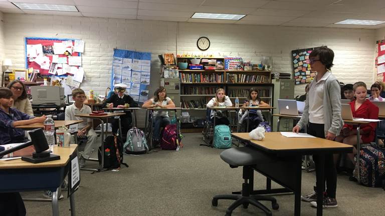 Young students sit at desks arranged in a semi-circle in a classroom