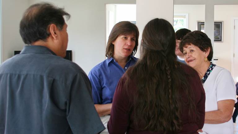 Four adults stand in a room and talk with one another