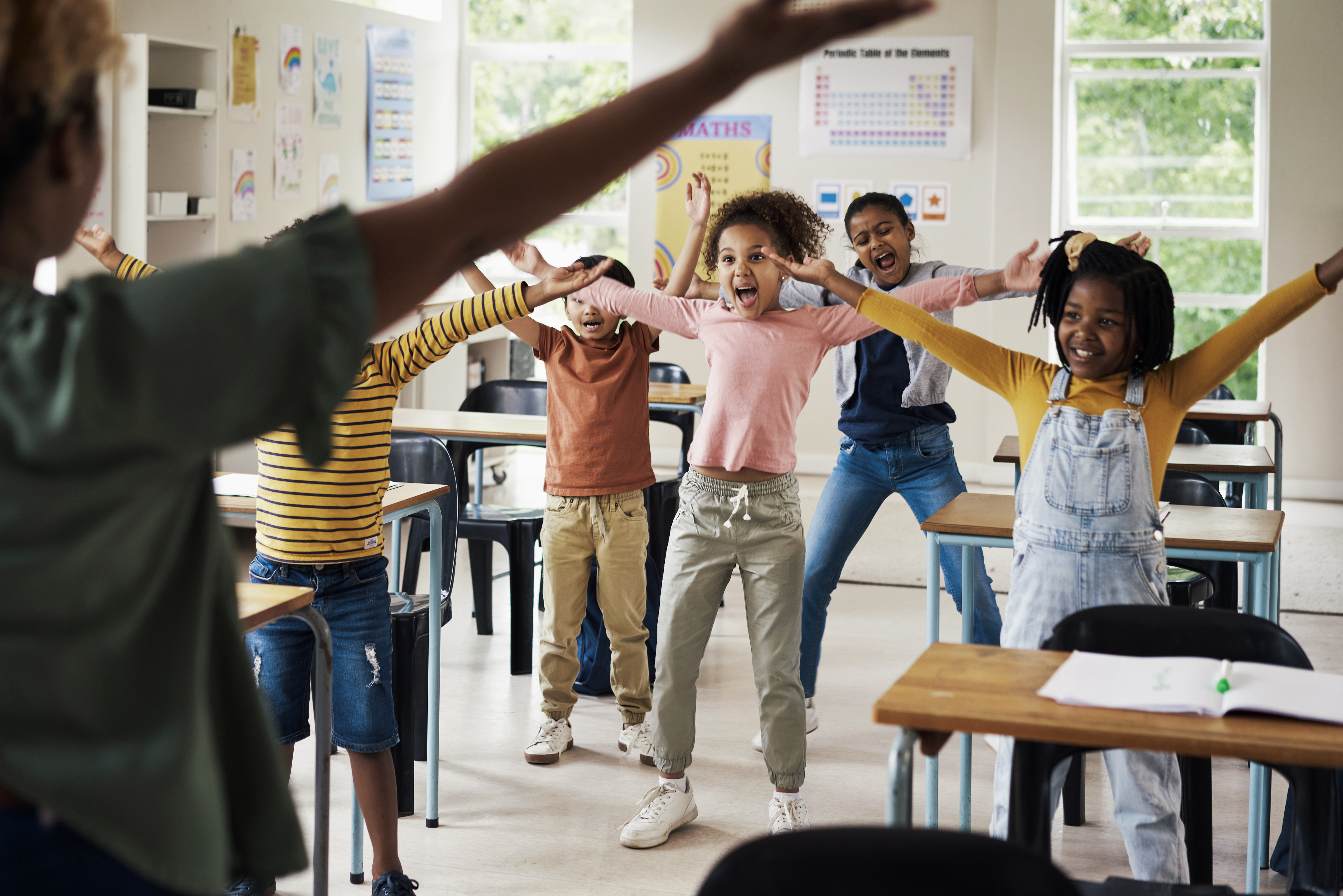 Students in a classroom following a teachers movement patterns. They are stretching and moving with energetic and happy looks on their faces.