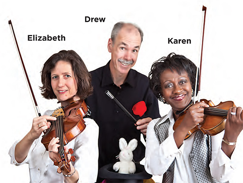 From left to right: a white woman with short brown hair wearing a white shirt holding her viola up to her chin; a balding tall white man with a gray moustache wearing a black shirt with a red pocket square holding a magic wand and stuffed white rabbit in a top hat; and a Black woman with short brown hair wearing a white shirt and silver checkered vest holding her violin up to her chin. All are smiling.
