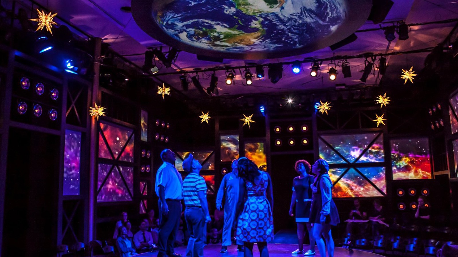 Actors reach up toward an overhead image of the earth in Earthrise