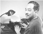A photo of a Langston Hughes sitting at a desk with his hands posed on a typewriter.