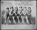 A black-and-white photo of six Black chorus line performers in matching romper outfits, top hats, and shoes. The performers pose in a single line, standing in a wide stance. Each performer grips the top of a cane in both hands, and their canes are positioned in front of them.