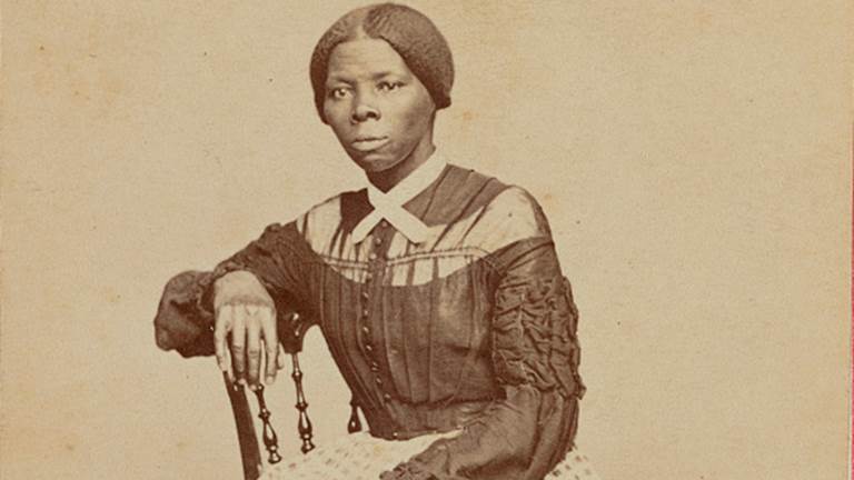 A sepia-colored photograph of Harriet Tubman. She is sitting in a chair with her arm resting on the back of the chair.