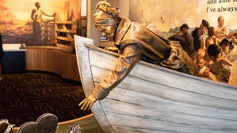 A bronze statue of Harriet Tubman in a boat. She is leaning over the boat helping a child out of the water. 