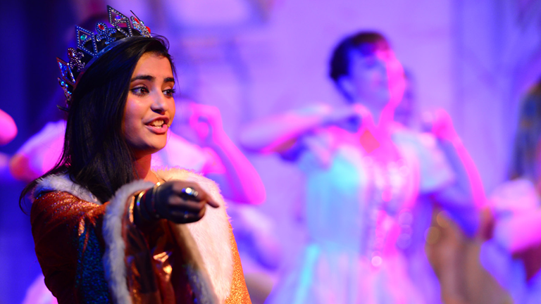 A girl wearing a crown gesturing with her right hand.