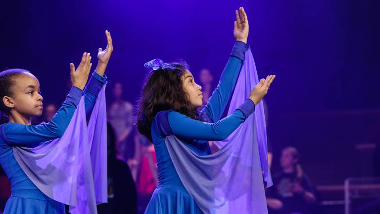 Two children purple costumes making dance motions with their arms.