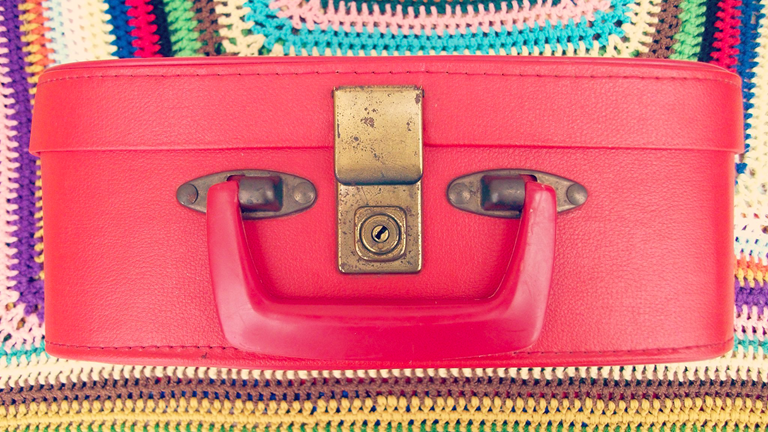 A red suitcase sitting on multi-colored crocheted blanket. 