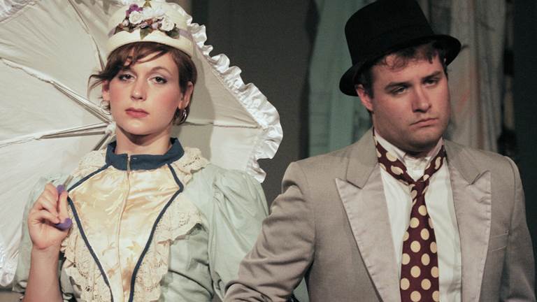 A scene from the play The Hairy Ape. A woman with an umbrella locks arms with a man in a suit.