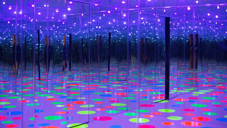 Yayoi Kusama's "Infinity Dots Mirrored Room". Bright colored dots on a floor reflecting off of mirrored walls. 