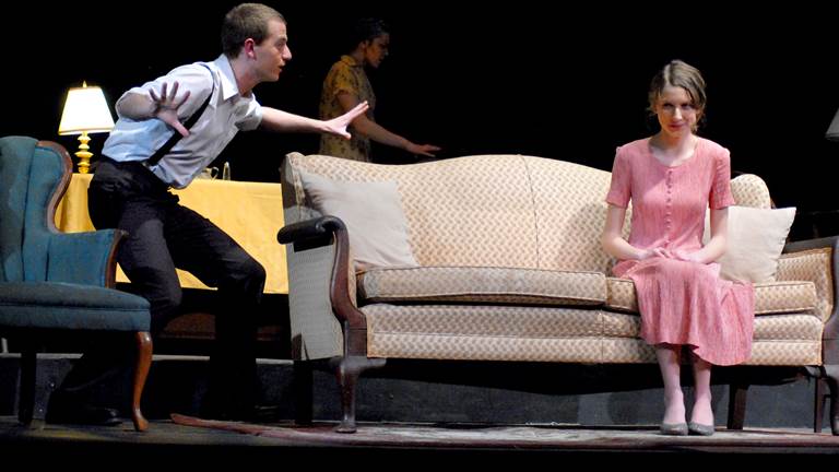 A scene from "The Glass Menagerie." A male character is speaking to a woman sitting on a sofa.  