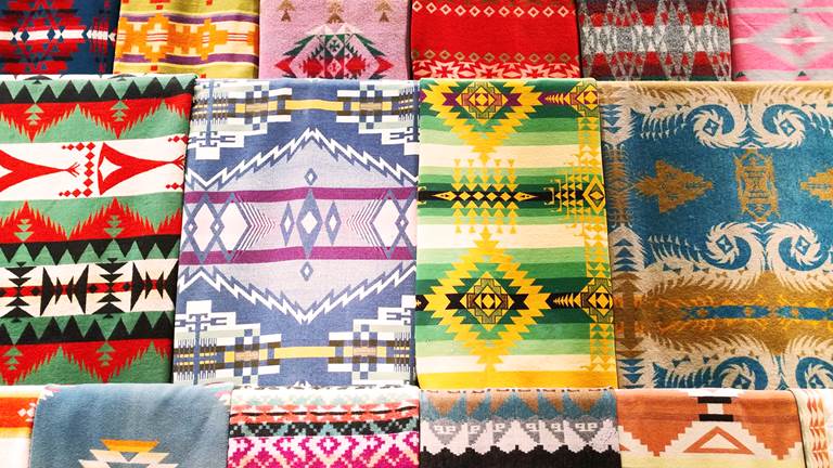 A wall decorated with a variety of Navajo blankets with different patterns and colors. 