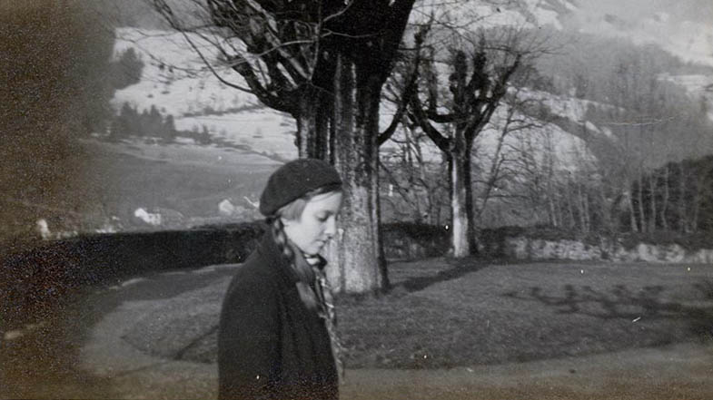A vintage of author Madeleine L'Engle as a young girl, wearing a dark coat and matching dark hat. She is outside walking around Switzerland in the daytime.jpg