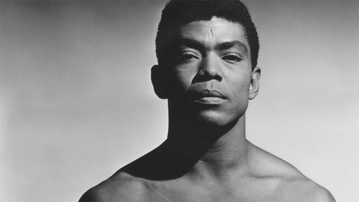 A black and white photo of a young man, dancer and choreographer Alvin Ailey, looking into the camera.