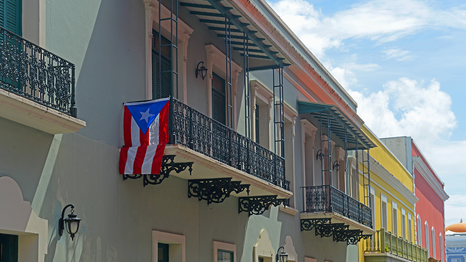 A row of colorfully painted two-story stucco buildings with wrought iron balconies. One balcony has a Puerto Rico flag hanging from it.