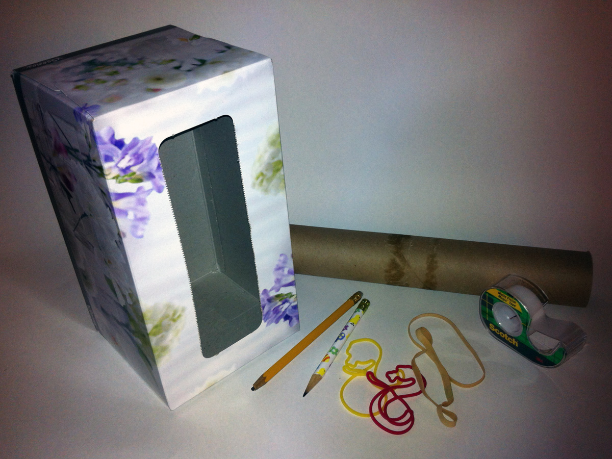 A photo of an empty tissue box, a paper towel roll, two pencils, a few rubber bands, and some tape.