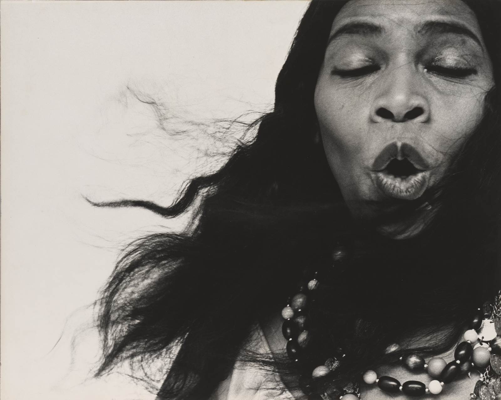 A close photograph of a woman's face, she has long black hair, closed eyes, and is singing