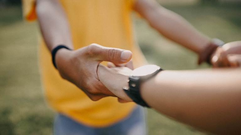 Two people hold hands, keeping their arms stretched in front of them. 