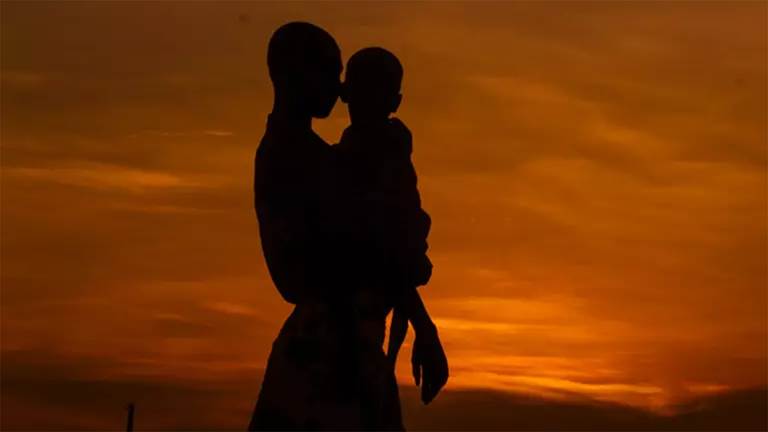 A photo of the silhouettes of an adult holding a child while looking at a sunset