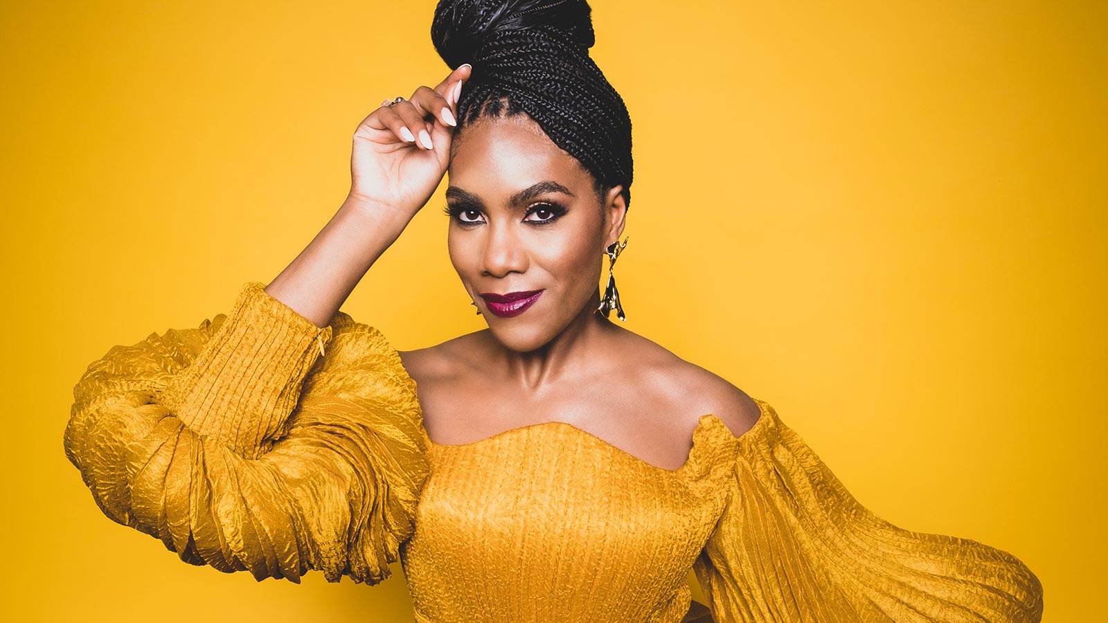 J'Nai Bridges in yellow dress on yellow background smiling