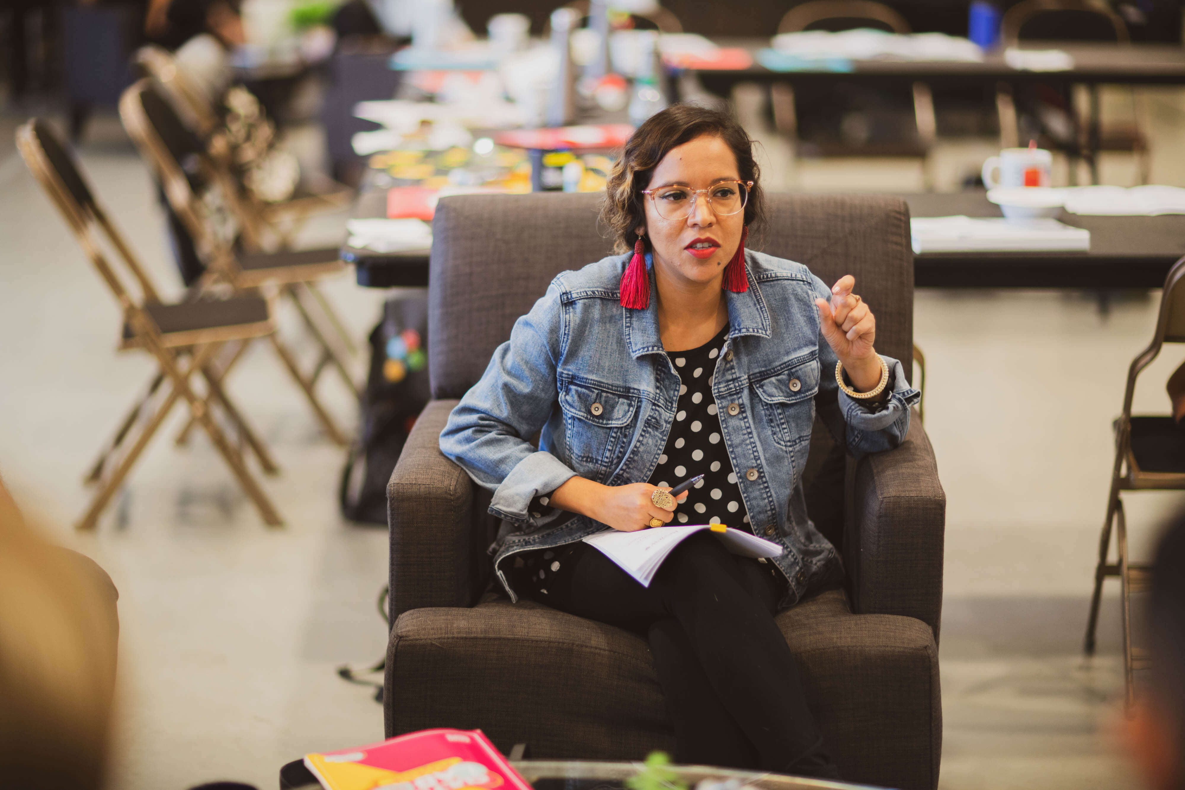 A woman talks while sitting in a chair with pen and paper