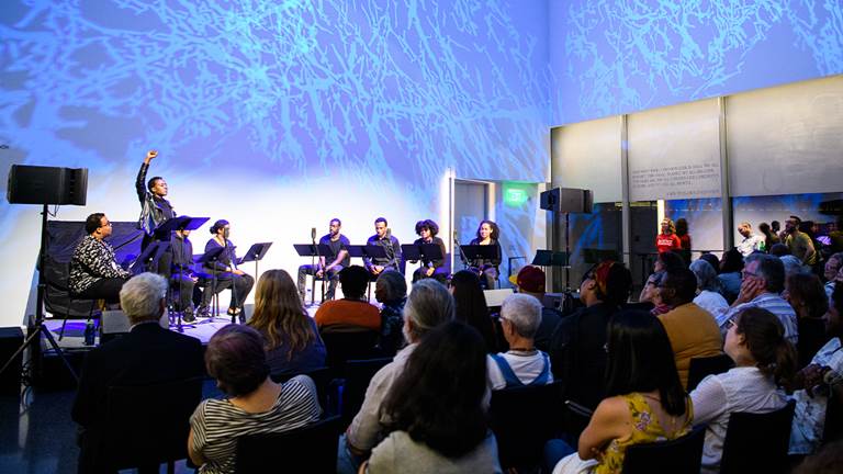 A photo of a Social Impact event with a panel onstage including a woman raising her fist. 