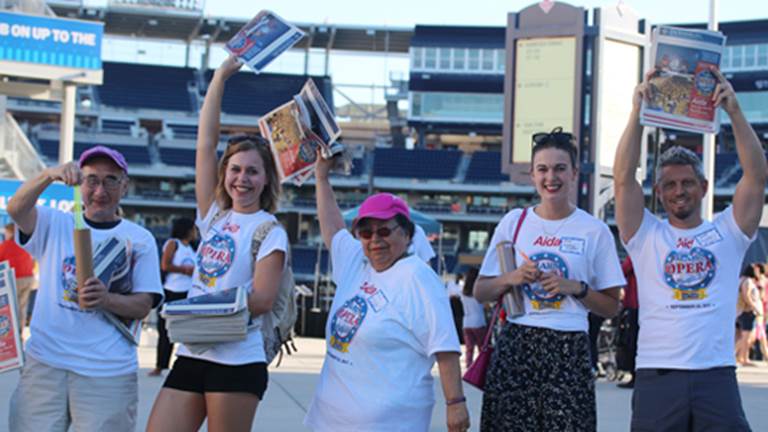 A group of volunteers handing out flyers for Opera in the Outfield.