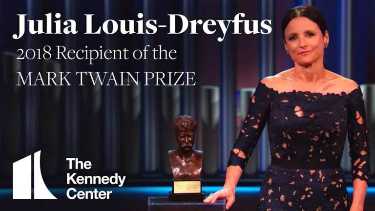 Comedian Julia Louis-Dreyfus wearing a black dress looks into the camera with a bust of Mark Twain next to her.