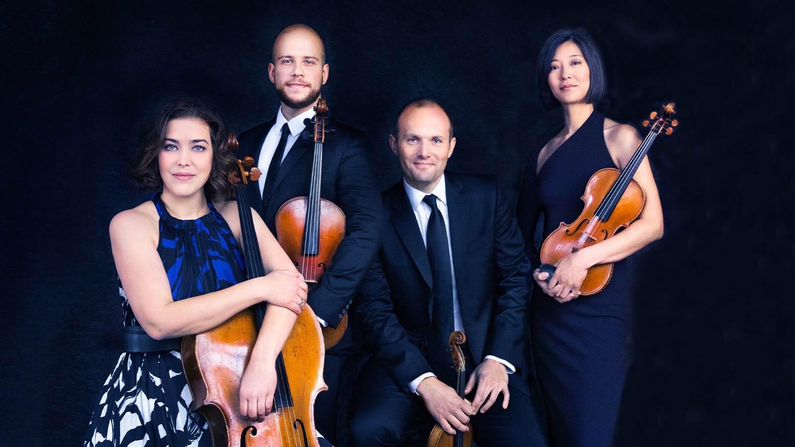 Artist of Quartet standing in front of a black background. Each artist is holding their string instrument.