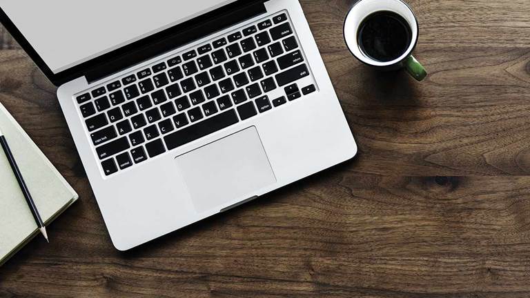 A laptop and coffee mug on a wooden table.