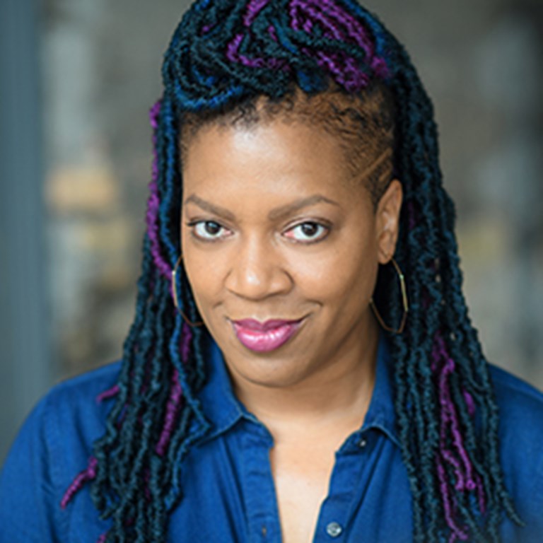 Lili-Anne Brown with navy, purple, and black wrapped dreadlock and a cocky smiles