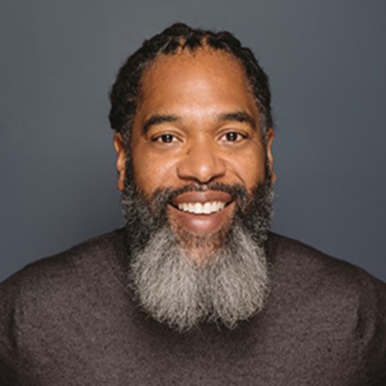 Randy Preston smiling with a greying bread trimed by his temples and touched up locs