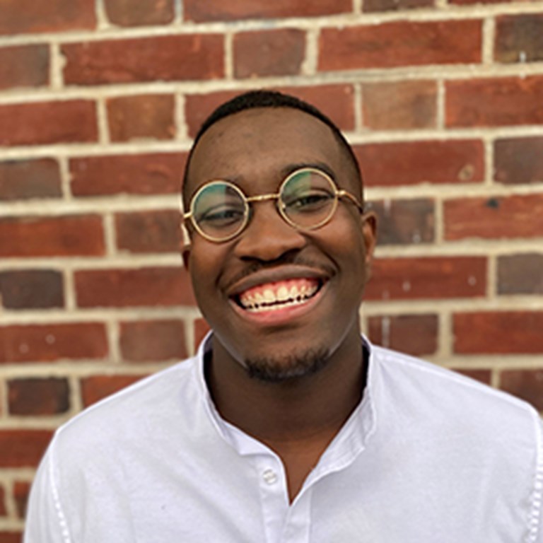 Terence David Odonkor smiling and wearing gold rimmed glasses