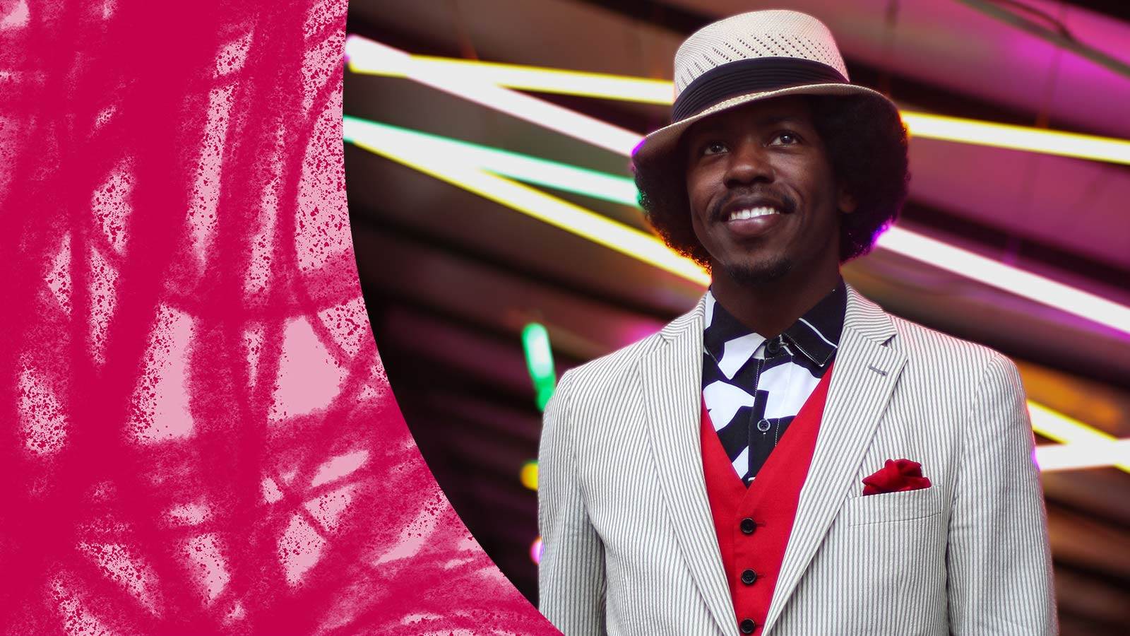 Christyles Bacon standing in white pinstripe suit in front of neon lights