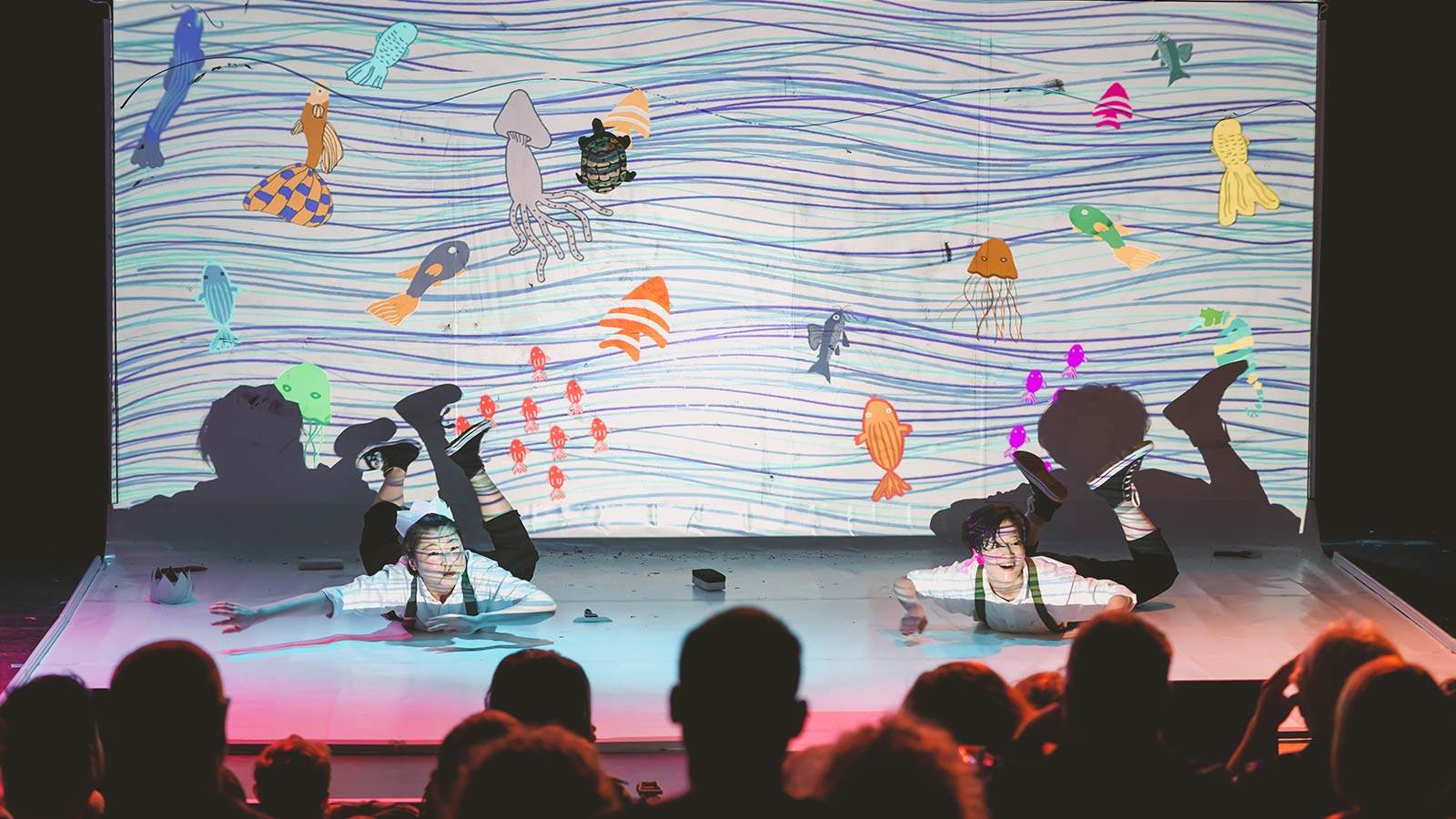 performance of Doodle POP with audience in foreground and two people on stage with projections