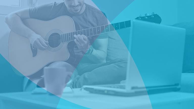 Man playing guitar on couch with laptop computer