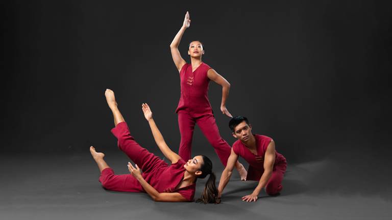 3 Dana Tai Soon Burgess Dancers in dynamic poses. They are wearing tailored red clothing and are in front of a grey background.