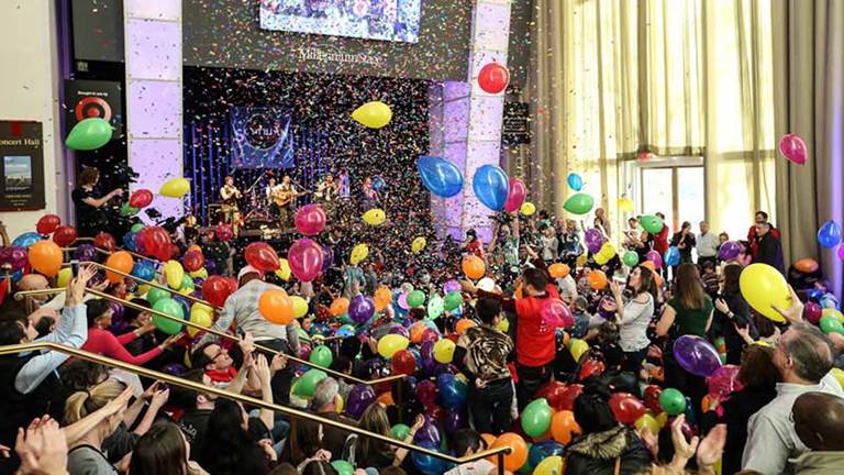 Millennium Stage 20th Anniversary Celebration with a crowd of people enjoying falling confetti and balloons. Photo by Jati Lindsay