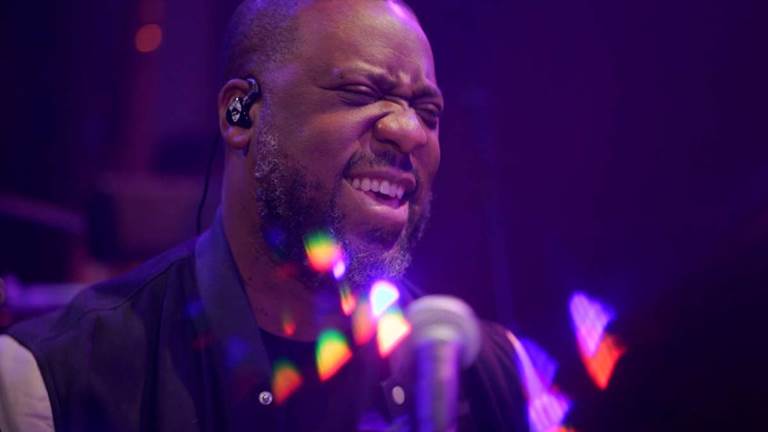 Robert Glasper smiles as he performs in a blue light.
