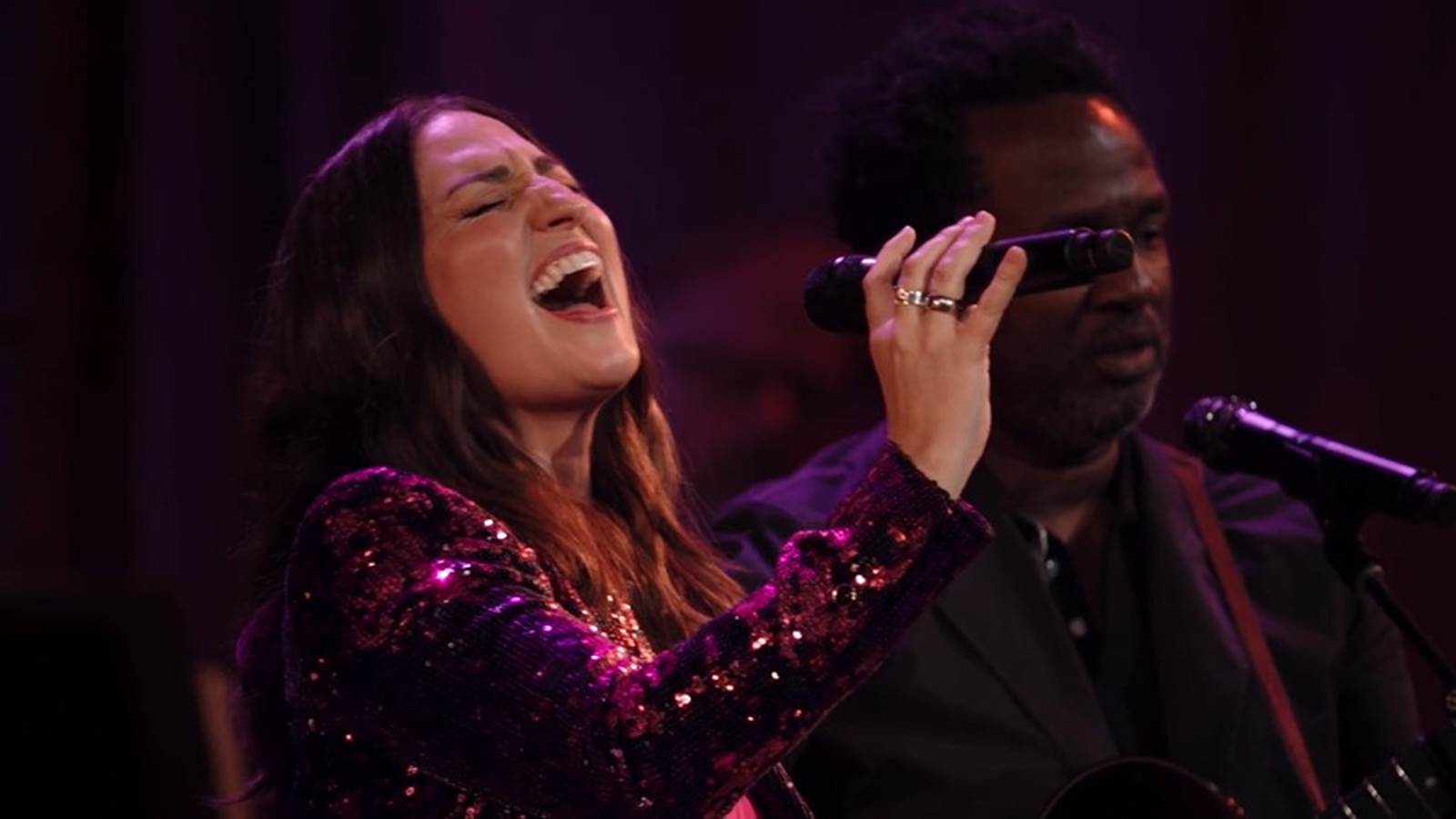 Sara Bareilles closes her eyes as she sings into a microphone with head tiled back.